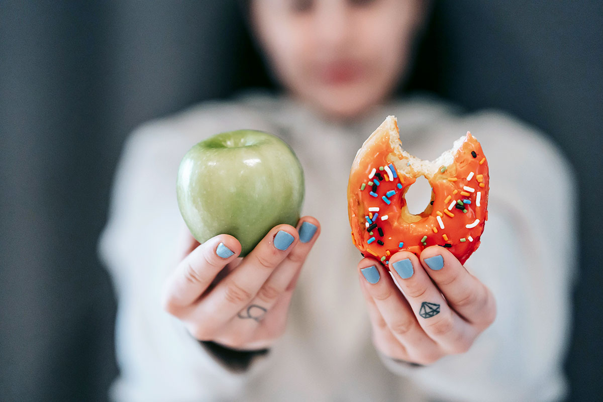 a woman holding an apple on the right hand and a donut on the other hand