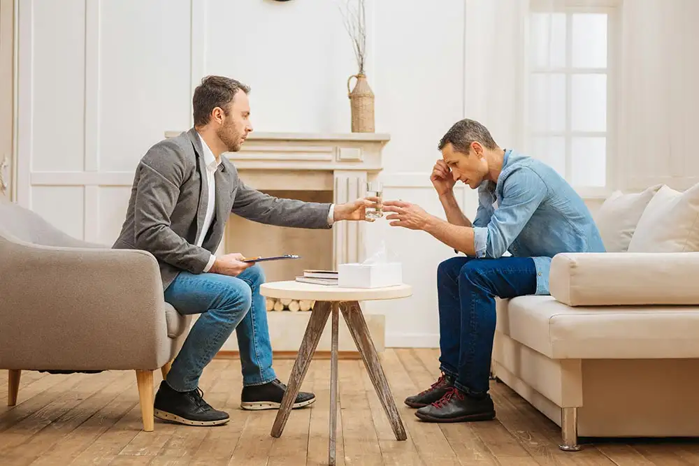 Two men seated on a couch in a living room during Prolonged Exposure Therapy