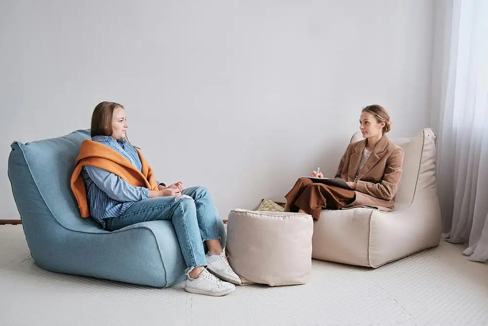 Two women engaged in a discussion on bean bags during Cognitive Behavioral Therapy in a cozy room setting