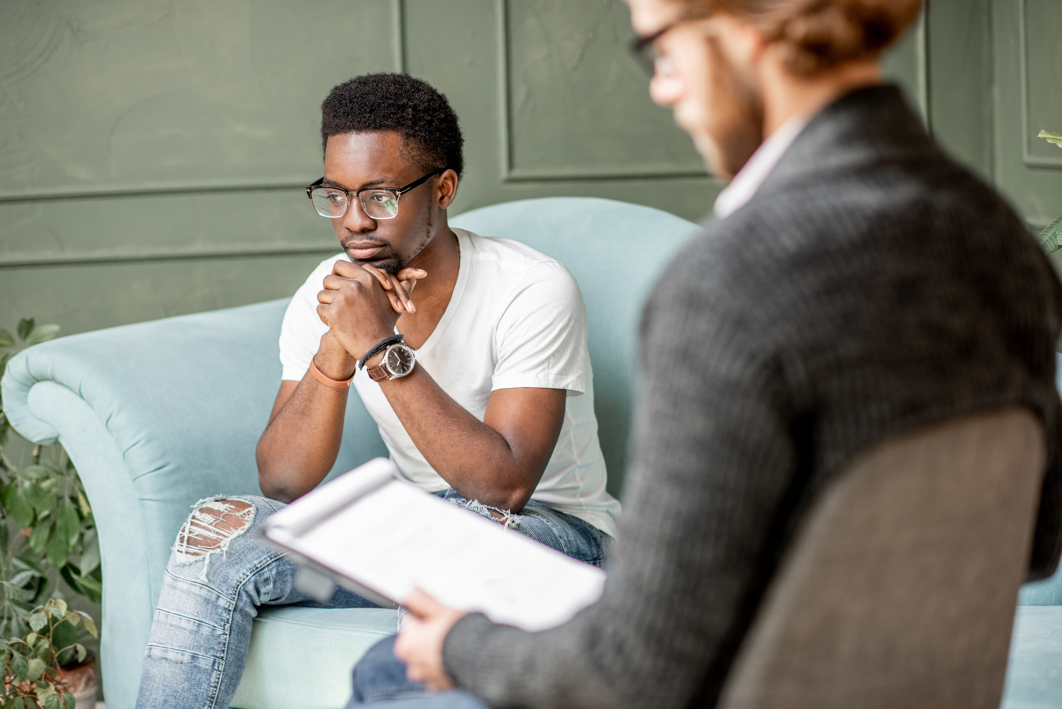 A man sits in an autism and depression therapy session, listening attentively while his therapist speaks.