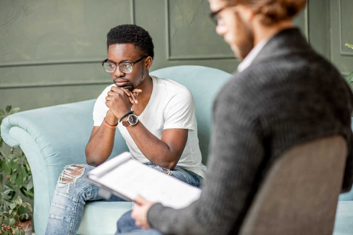 A man sits in an autism and depression therapy session, listening attentively while his therapist speaks.