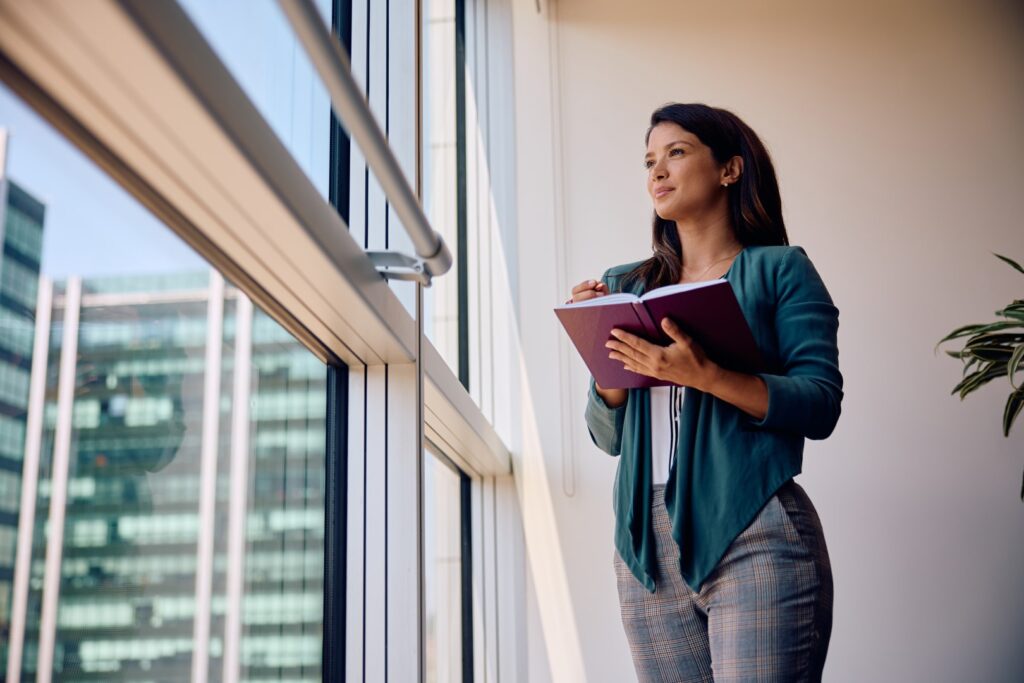 A professional woman standing thoughtfully near an office window