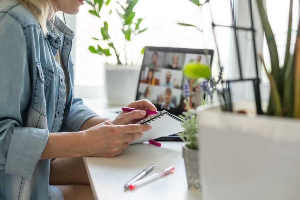 Woman attending online meeting with notepad and pe