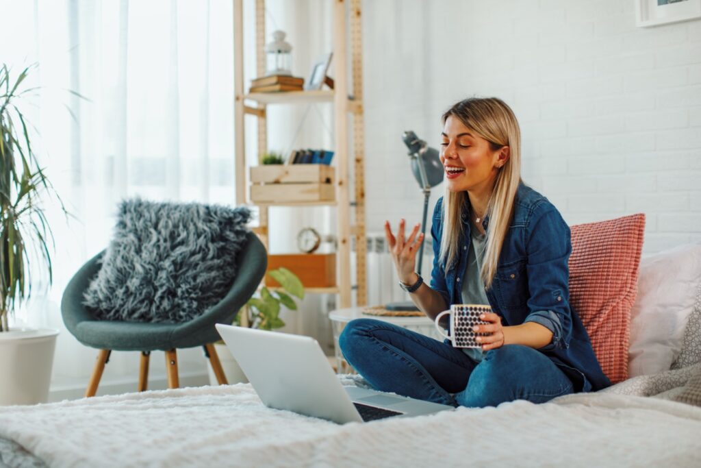 Woman chatting on laptop while sitting on bed
